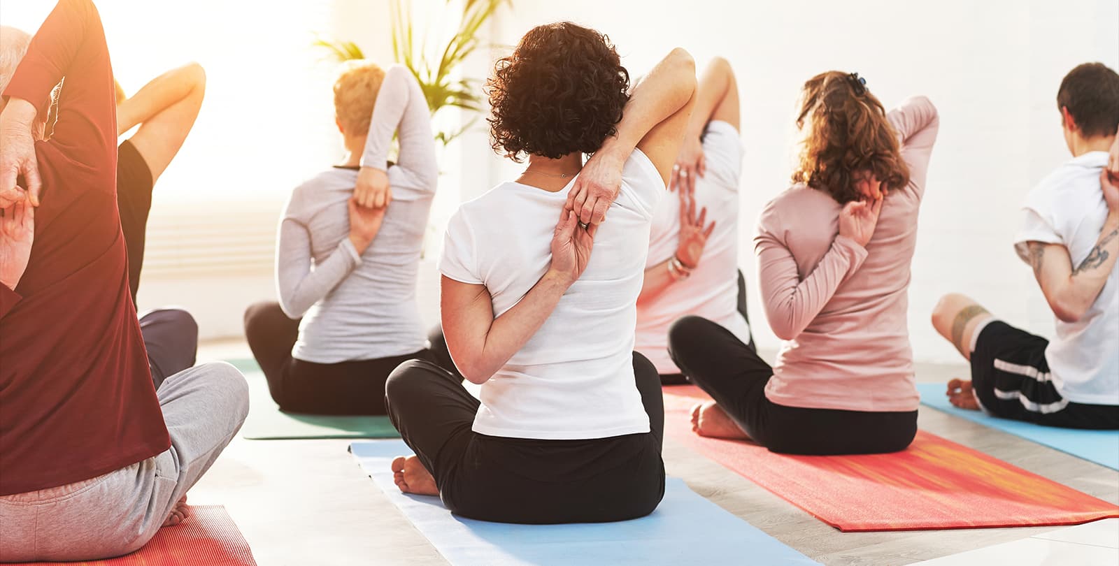 Frau mit lockigem Haar praktiziert Gomukhasana Yoga-Pose mit verschränkten Armen hinter dem Rücken im Gruppenkurs