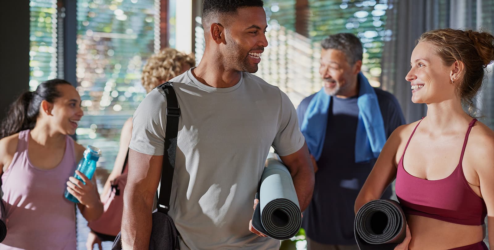Fröhliche Fitnessgruppe mit Yogamatten unterhält sich nach dem Training im Fitnessstudio